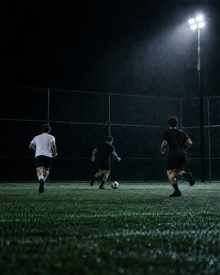 Three players chasing the ball on floodlit turf at night